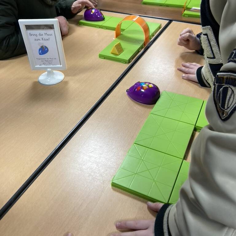 Kinderarme und Finger mit grünen, flachen Figuren auf einem Holztisch